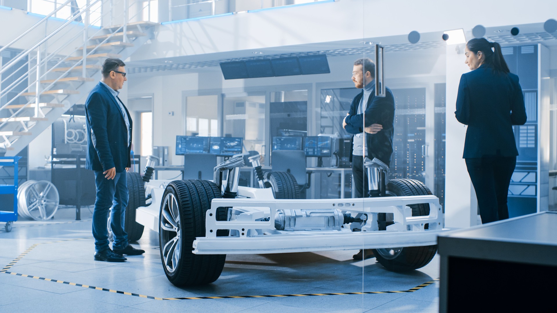Automotive Design Engineers Talking während der Arbeit am Elektroauto Chassis Prototyp. In der Innovation Laboratory Facility Concept Vehicle Frame beinhaltet Räder, Hängepartie, Motor und Batterie.